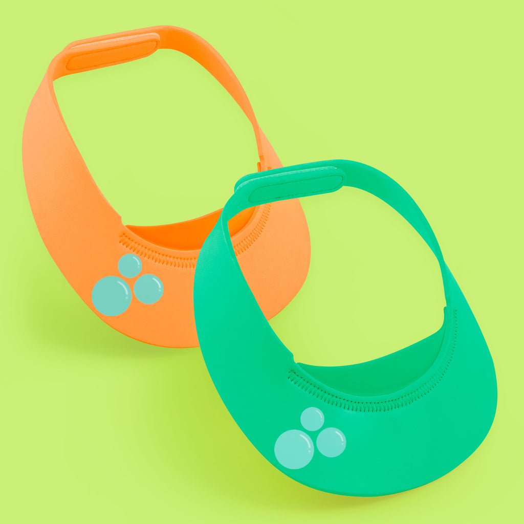 two foam visors (green and orange) with a velcro clasp to secure the visor on baby's head. the visors have three bubbles illustrated on the front. 