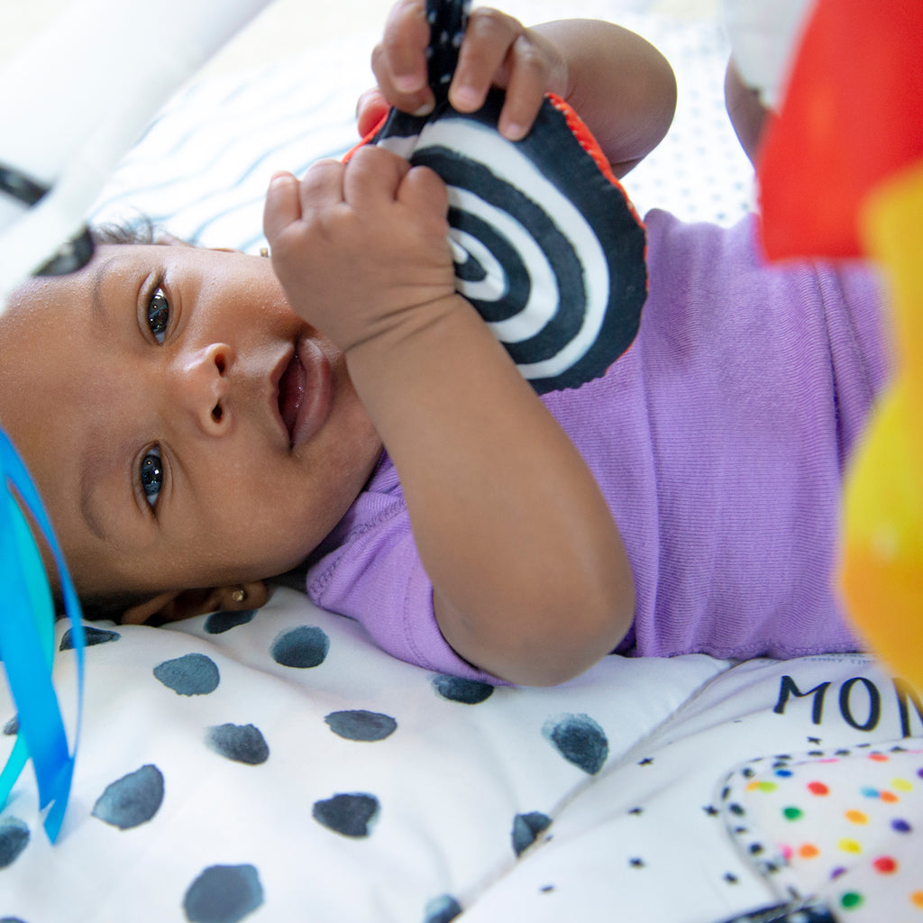 infant laying on milestone playmat, holding pillow toy