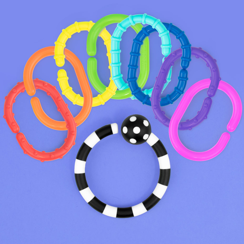 a 9 piece ring set with 8 rainbow ordered rings with different textures. they loop around a black and white striped ring with a black and white polka dot ball.