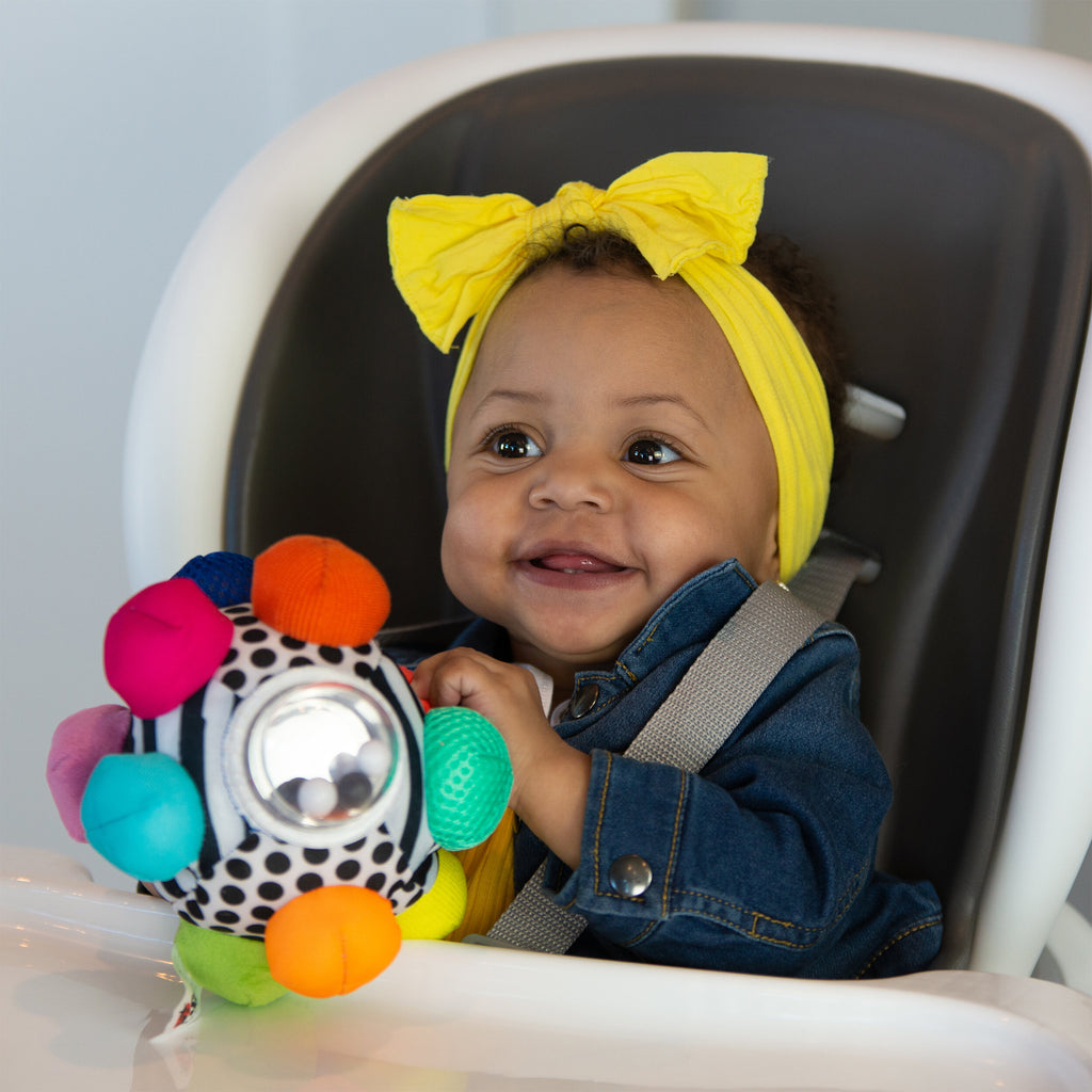 baby playing with black and white plush ball with multicolored bumps coming off of the ball. 