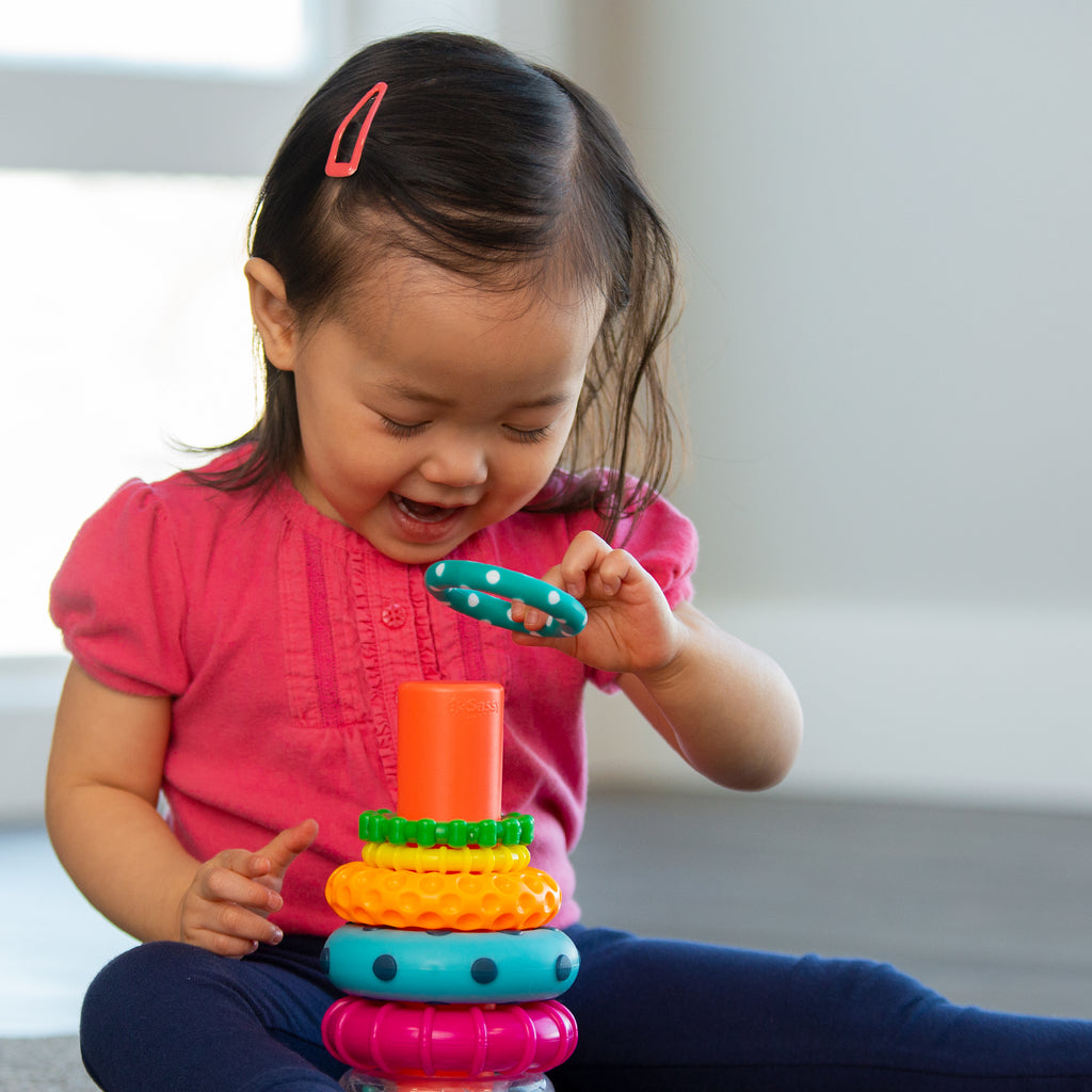 toddler sitting on the floor, playing with the Sassy stacks of circles toy