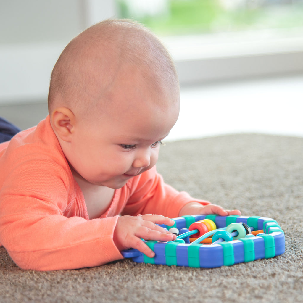 infant girl laying on floor, smiling, looking at sassy busy bands toy