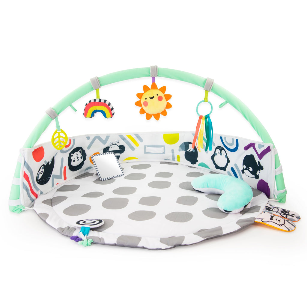 playmat with gray polka-dots, an arch with toys on it, a bolster, and floor mirror