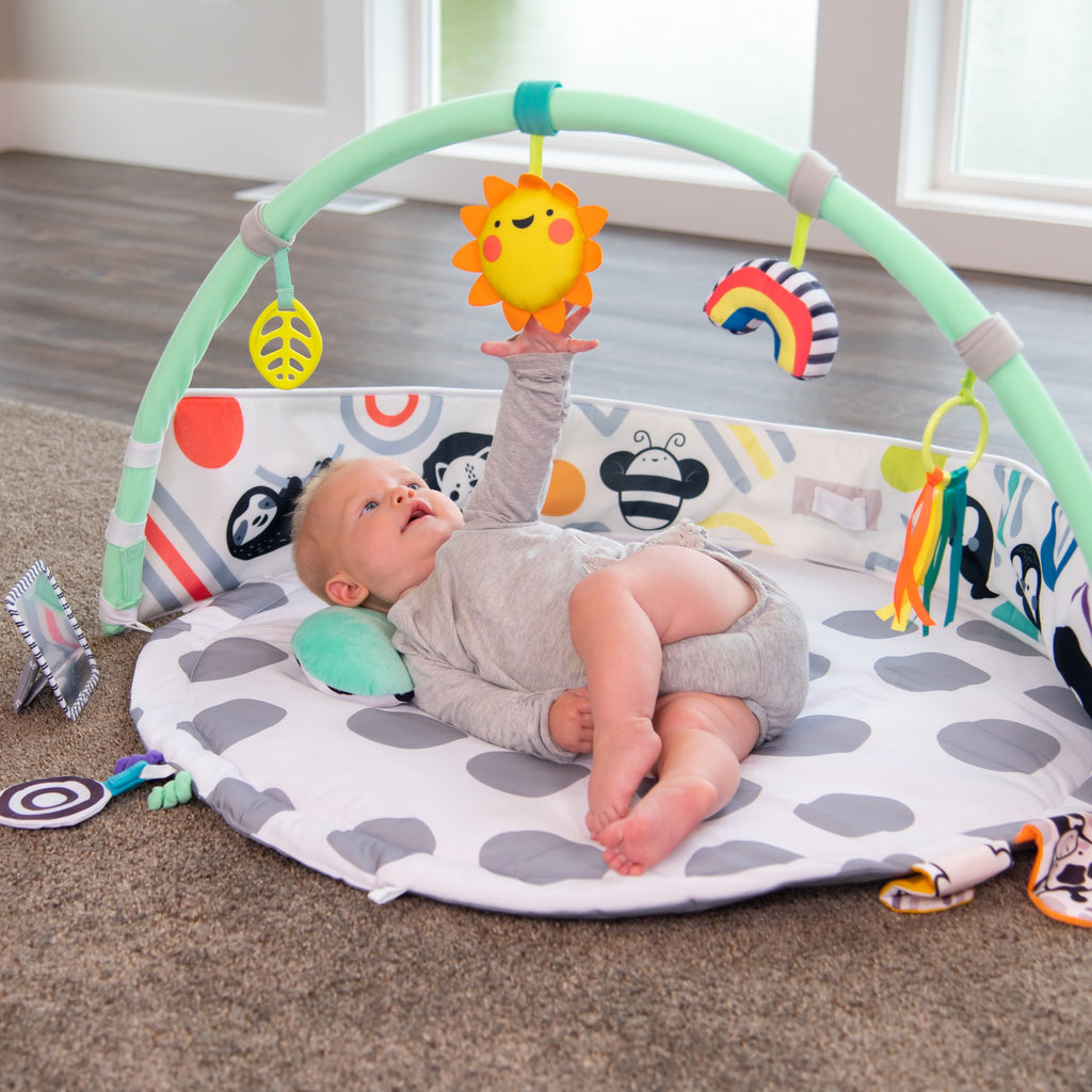 baby laying on playmat reaching up at a toy toward arches