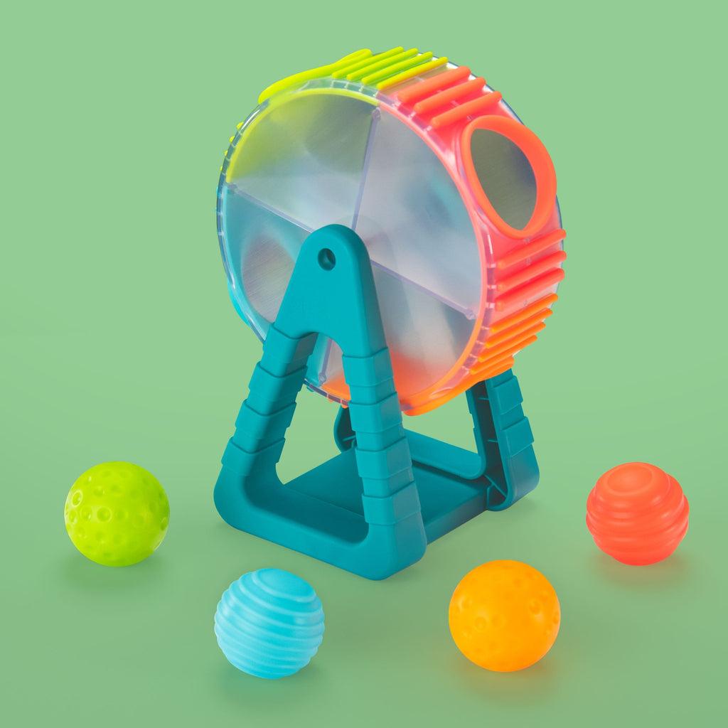 a flat sphere with a multi-colored and ridged border that has 4 holes around it that is being held up between two blue triangular stands with flat bottom. it comes with 4 different colored and textured balls that you can drop in the holes, spin it, and the balls will come out.