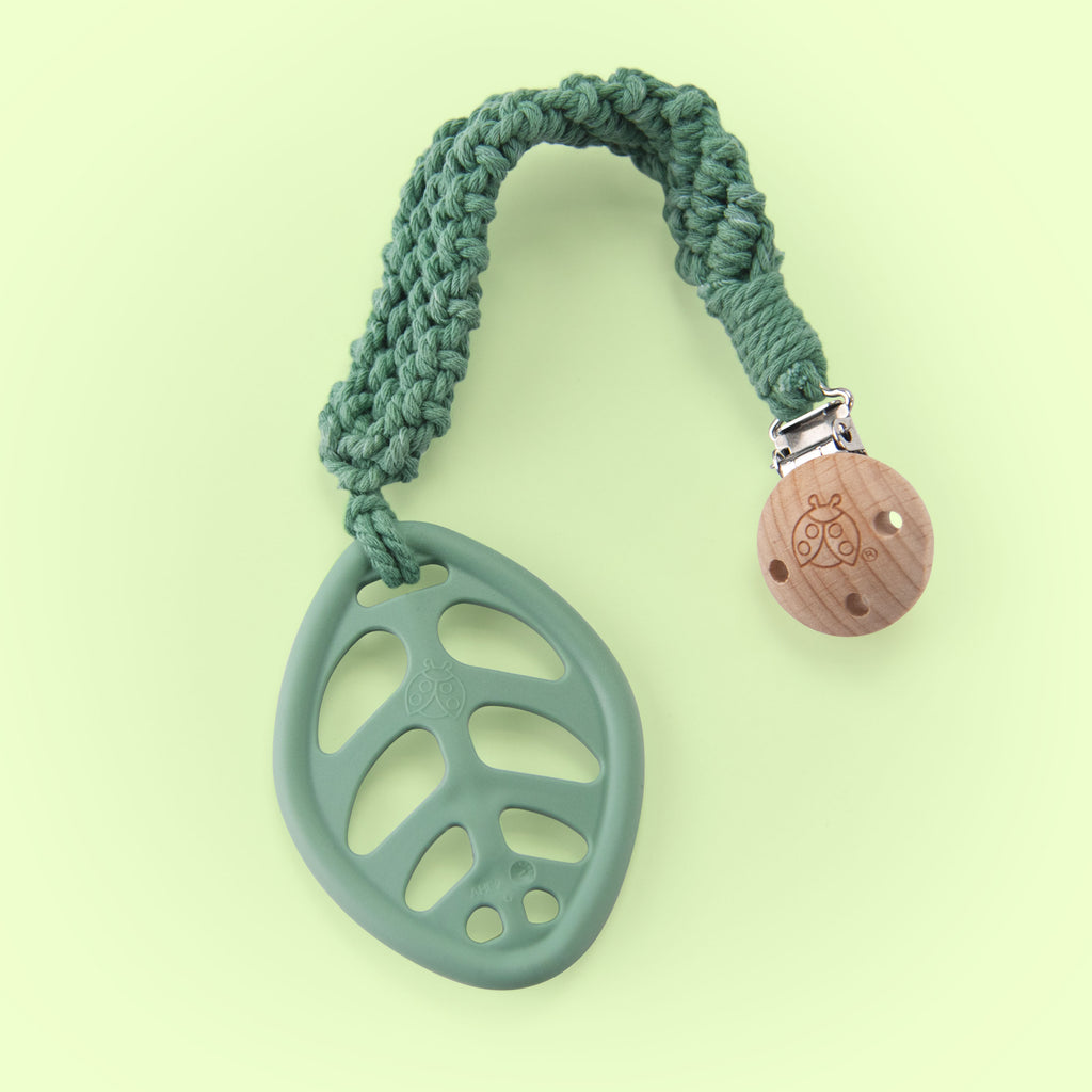 sage green knit strap with a green leaf shaped teether at the end. it has a wooden clip on the other end to attach "on the go" 