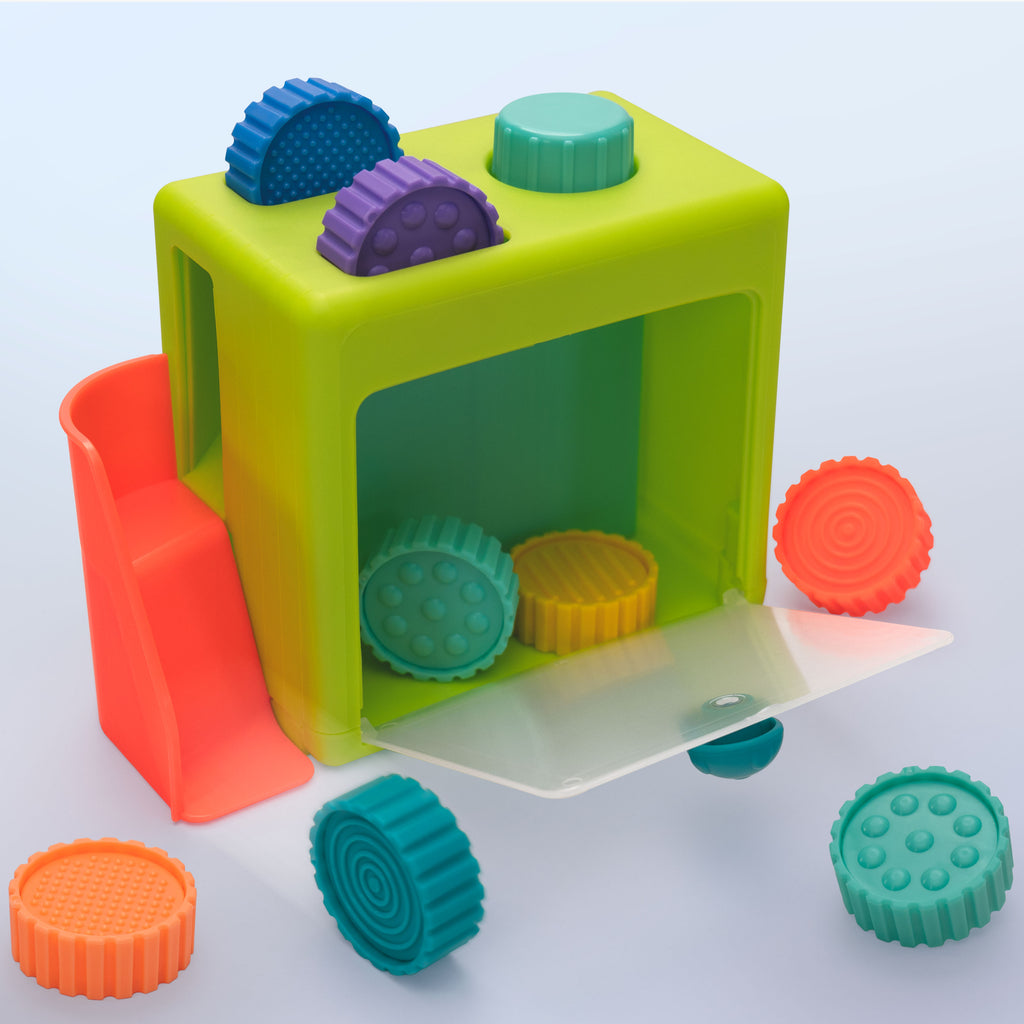 Green coin drop cube with a clear front door, two top coin slots, a colored button, and a red/pink slide for coins. Includes eight multicolored coins, each about an inch thick