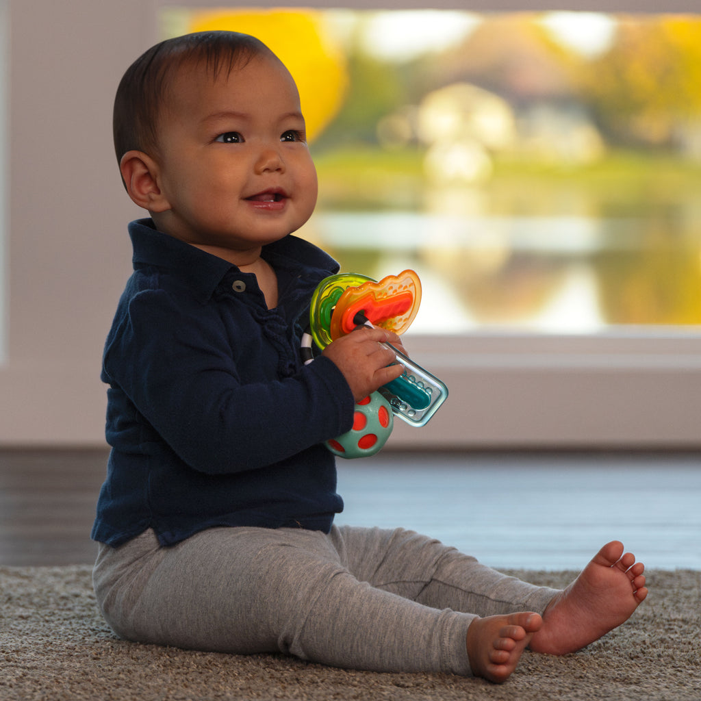 infant girl sitting on floor, holding drive n' drool keys, smiling.