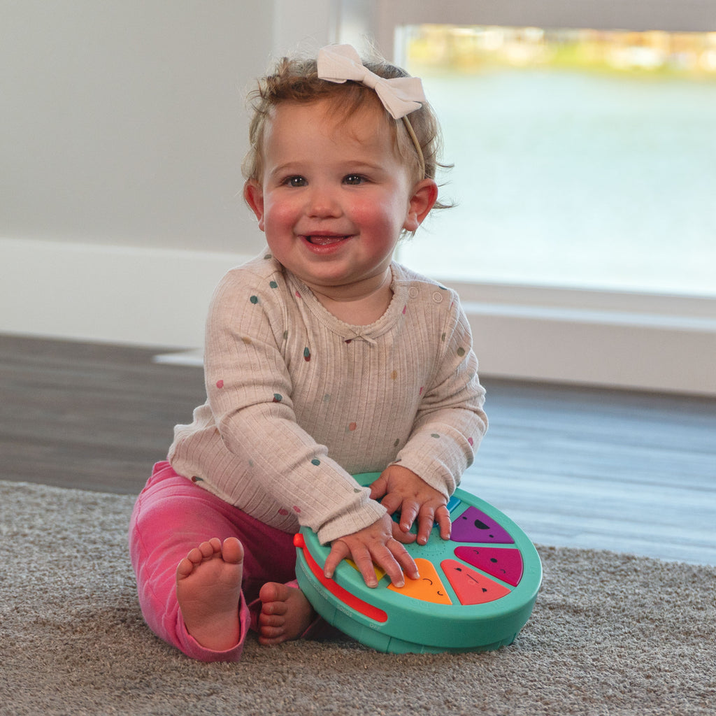 infant girl sitting on the floor, smiling, playing with piano of personalities toy