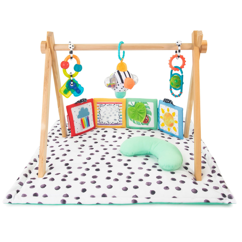 a black and white polka dot tummy time play mat (flipped over is turquoise) with wooden arches that go over the mat. includes 5 different toys including: multi-colored teethable keys, a black and white patterned ball with different colored bumps, a multi-colored loopy rattle with a textured ball in the middle, a multi-textured/colored sensory a turquoise bolster. 
