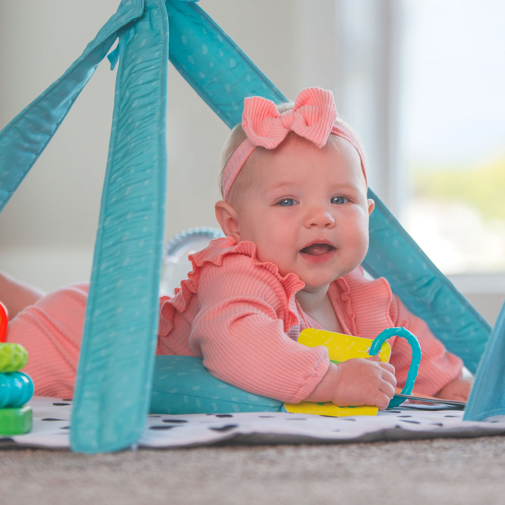 Baby laying on tummy under the arches of playmat holding on to toy