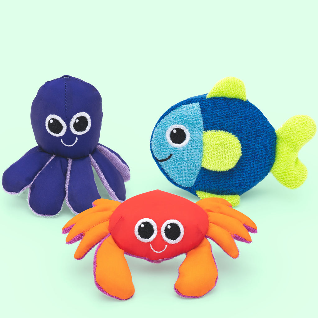 three soft multi-fabric textured ocean themed bath toys. a purple octopus with loose tentacles and googly eyes. there is a blue and green fish with loose fins and googly eyes. lastly a red, orange, and pink crab with loose legs and claws with googly eyes. 