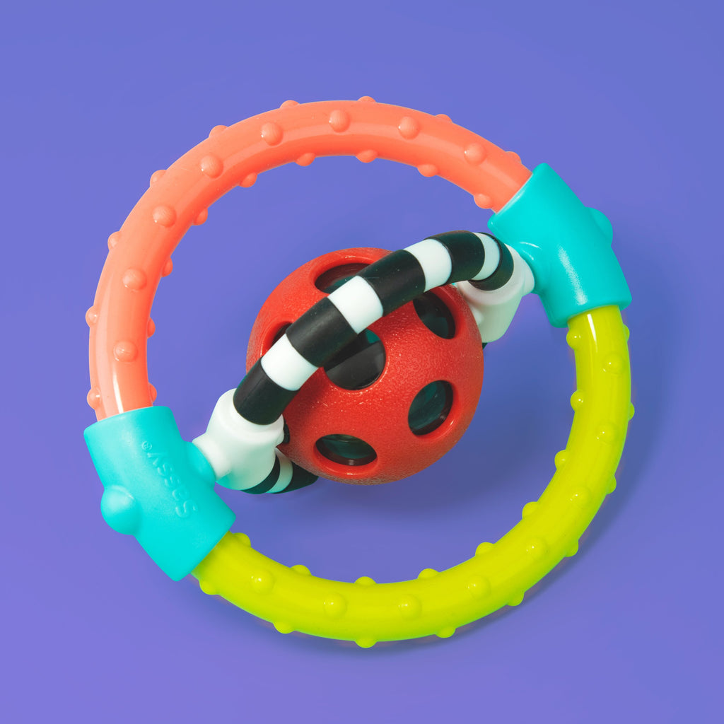 a circle ring shaped teether with multiple colors and textures. there are two blue pieces on the side that secure a red and black polka dot ball & black and white striped ring in the middle. the ring and ball spin