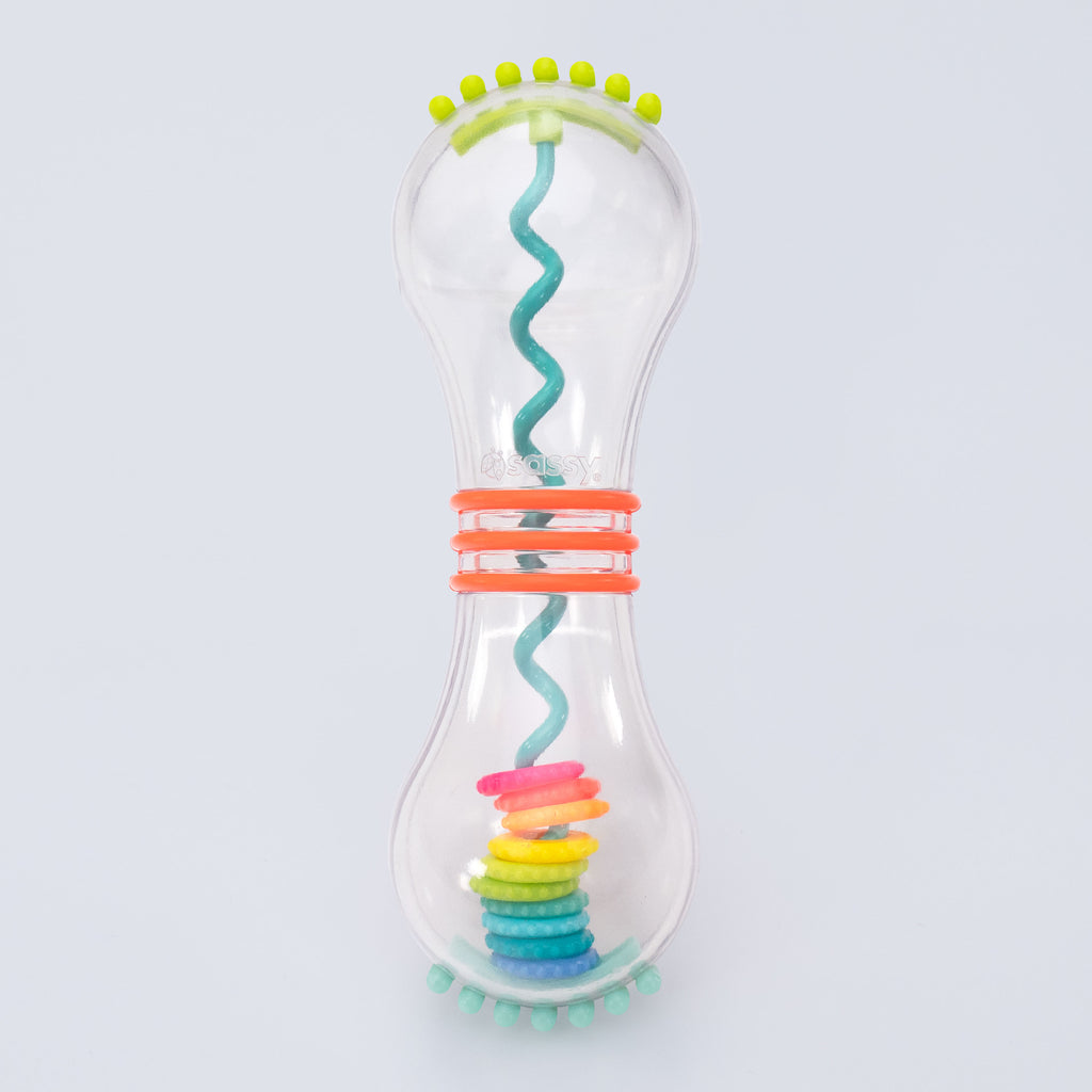 a clear hourglass shaped rattle with a blue spiral inside with rainbow ordered rings stacked on top of each other/ when you turn the rattle upside down, the rings spiral down. the rattle has green ridges on the top, blue ridges on the bottom, and three orange ridges on the center on the rattle. 