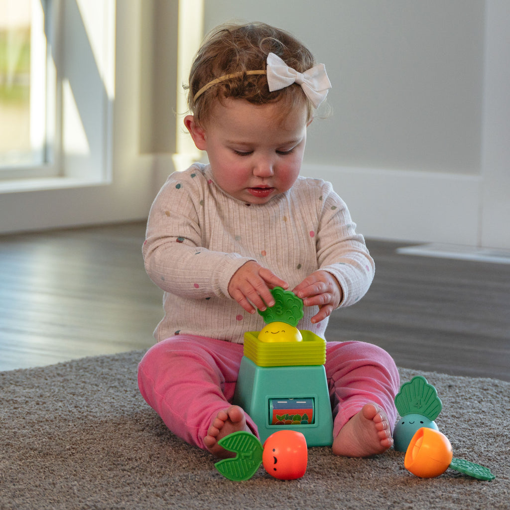 infant girl sitting on floor, playing with veggie scale toy